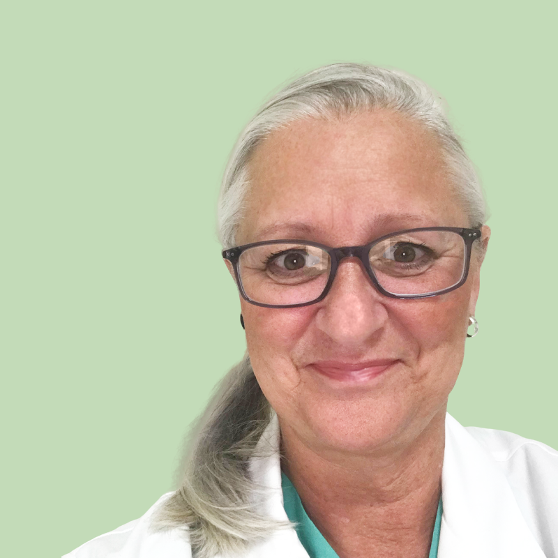 A person with glasses and a white coat smiles in front of a light green background.