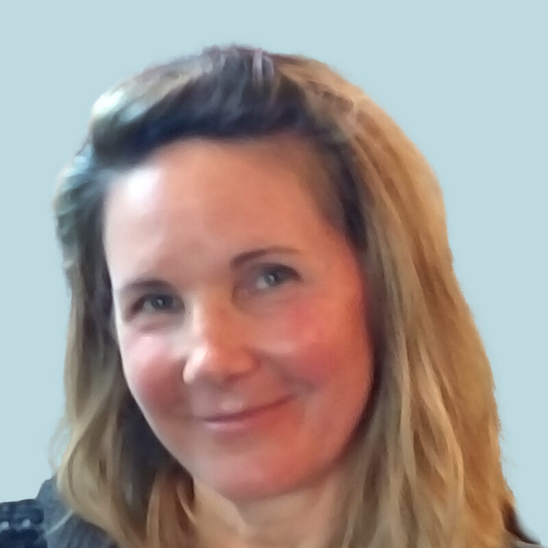 Woman with light brown hair smiling at the camera against a plain background.