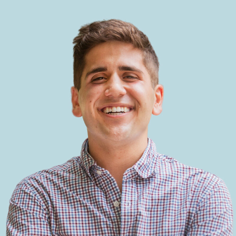 Young man smiling, wearing a checkered shirt against a light blue background.