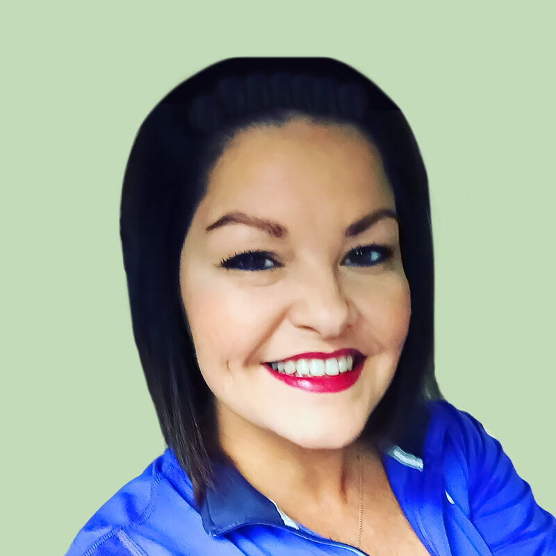 A person with shoulder-length dark hair smiles while wearing a blue top against a light green background.