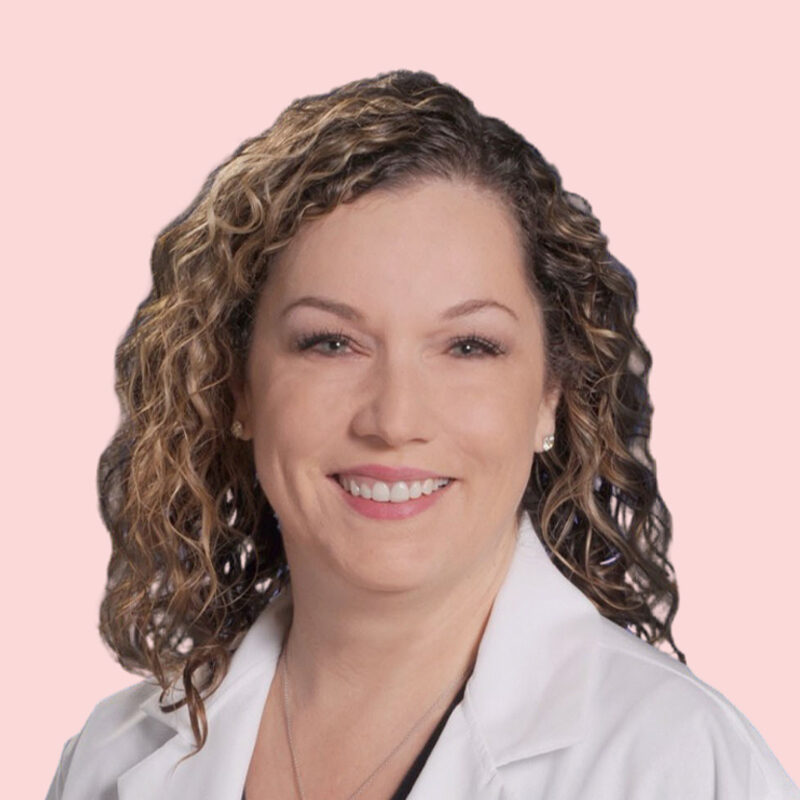 Smiling woman with curly hair in a white coat against a pale pink background.